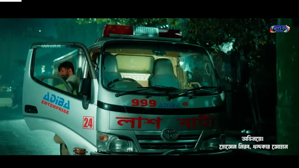 A man stands beside the open door of an ambulance-style body transport vehicle at night in Harami.