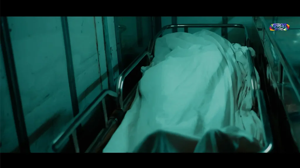 A body covered with a white sheet lies on a metal hospital stretcher in a dark scene from Harami.