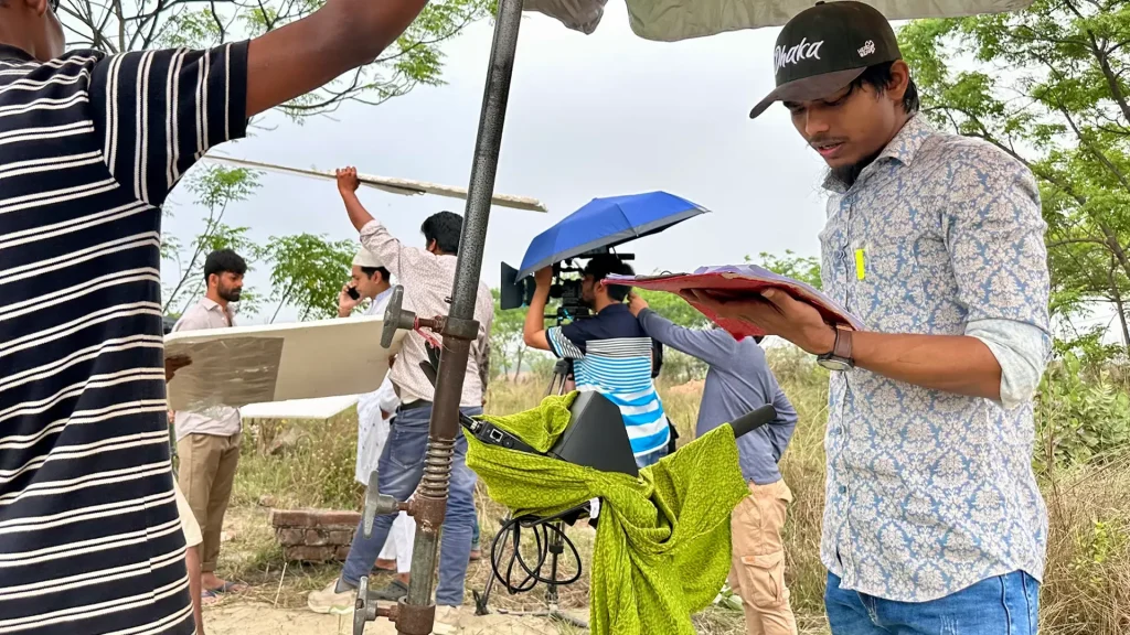 Director Faisal Khan Shuvo prepares an outdoor Harami scene while a crew member reviews the shooting script.